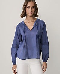 A woman wearing a blue long-sleeved blouse and white pants stands against a plain, light-colored background. carousel Product Image 1