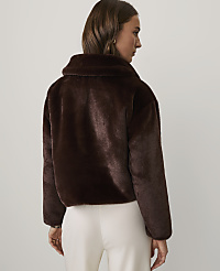 A woman wearing a dark brown faux fur jacket and white trousers stands against a plain white background. carousel Product Image 2