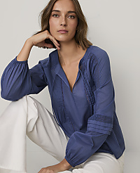 A woman wearing a blue long-sleeved blouse and white pants poses against a plain white background. carousel Product Image 3