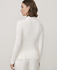 A woman wearing a white ribbed turtleneck sweater and white pants stands against a plain, light-colored background. carousel Product Image 2