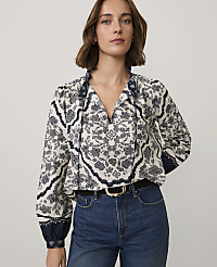 A woman wearing a patterned white and navy blouse and blue jeans stands against a plain light gray background. carousel Product Image 1