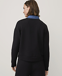 A woman wearing a black sweatshirt over a blue denim shirt stands against a plain, light-colored background. carousel Product Image 2