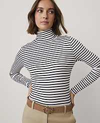 A woman wearing a navy and white striped turtleneck and khaki pants stands against a plain light gray background. carousel Product Image 1