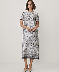 A woman wearing a patterned grey midi dress and beige heels stands against a plain white background. carousel Product Image 1