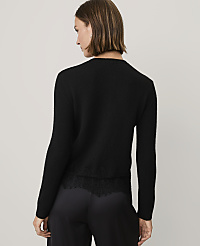 A woman wearing a black sweater with lace detailing and black trousers stands against a plain light gray background. carousel Product Image 2