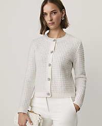 A woman wearing a white textured cardigan and white trousers stands against a plain, light-colored background. carousel Product Image 1