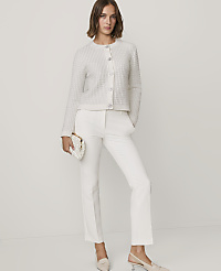 A woman wearing a white textured cardigan, white trousers, and beige heels stands against a plain white background. carousel Product Image 3