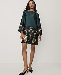 A woman wearing a green and black patterned dress and black heels stands against a plain white background. carousel Product Image 1