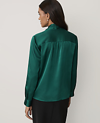 A woman wearing a green satin shirt and black trousers stands against a plain light gray background. carousel Product Image 2