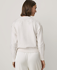 A woman wearing a white lace-detailed sweater and matching trousers stands against a plain light gray background. carousel Product Image 2