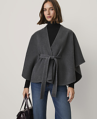 A woman wearing a grey wrap, black turtleneck, and blue jeans stands against a plain light-colored background. carousel Product Image 1