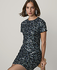 A woman wearing a sparkling blue and black sequined dress sits on a wooden chair against a plain light gray background. carousel Product Image 3