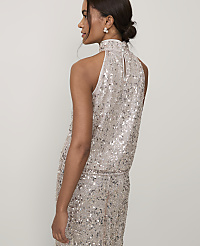 A woman wearing a shimmering, sequined silver dress stands in profile against a plain, light-colored background. carousel Product Image 2