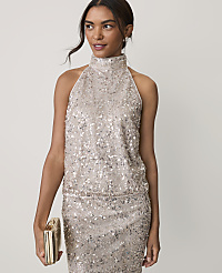 A woman wearing a shimmering, sequined two-piece outfit and holding a gold clutch stands against a plain, light-colored background. carousel Product Image 1