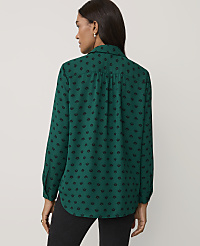 A woman wearing a green patterned shirt and black trousers stands against a plain, light-colored background. carousel Product Image 2