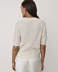 A woman wearing a cream-colored textured short-sleeved sweater and white satin trousers stands against a plain light gray background. carousel Product Image 2
