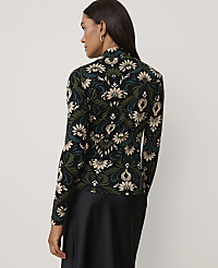 A woman wearing a floral patterned top and a black skirt stands against a plain light gray background. carousel Product Image 2