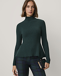 A woman wearing a dark green ribbed peplum sweater and plaid trousers stands against a plain light gray background. carousel Product Image 1
