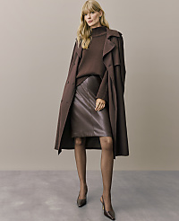 A blonde woman wearing a brown sweater, leather skirt, and long coat stands against a plain, neutral-toned background. carousel Product Image 6