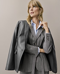 A blonde woman wearing a pinstriped grey suit and light blue shirt with a dark grey leather jacket draped over her shoulders stands against a plain beige background. carousel Product Image 6