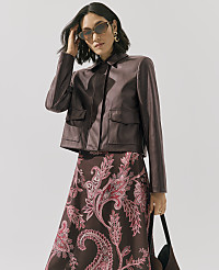 A woman wearing a brown leather jacket and a paisley-patterned skirt stands against a plain light gray background. carousel Product Image 5