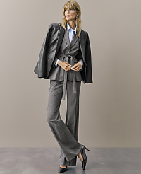 A woman wearing a grey pinstripe suit and a black leather jacket draped over her shoulders stands against a plain, neutral-toned background. carousel Product Image 4