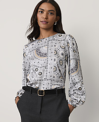 A woman wearing a patterned grey blouse and dark trousers stands against a plain white background. carousel Product Image 1