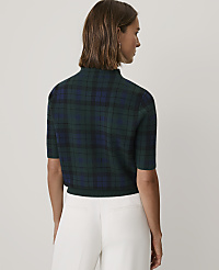 A woman wearing a green and blue plaid short-sleeved top and white trousers stands with her back to the camera against a plain light grey background. carousel Product Image 2