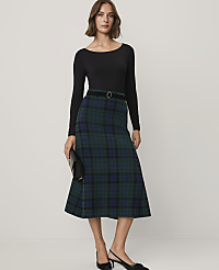A woman wearing a black long-sleeved top and a green plaid midi skirt stands against a plain, light-colored background. carousel Product Image 1