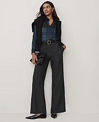 A woman wearing a blue plaid shirt, black vest, and wide-leg grey trousers stands against a plain, light-colored background. carousel Product Image 3