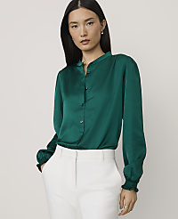 A woman wearing a green satin blouse and white trousers stands against a plain, light-colored background. carousel Product Image 1