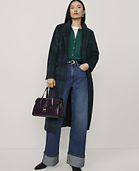 A woman wearing a green plaid coat, green cardigan, and wide-leg jeans stands against a plain white background while holding a dark purple handbag. carousel Product Image 1