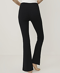 A person wearing black flared trousers and a white top stands against a plain, light-colored background. carousel Product Image 2