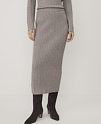 A person wearing a grey cable-knit sweater and matching midi skirt with dark brown ankle boots stands against a plain white background. carousel Product Image 2