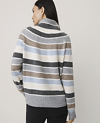 A woman wearing a multi-colored striped sweater and black pants stands against a plain, light-colored background. carousel Product Image 2