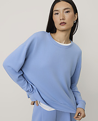 A woman wearing a light blue oversized sweatshirt and matching pants poses against a plain, neutral-colored background. carousel Product Image 1
