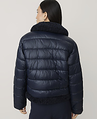 A woman wearing a navy blue puffer jacket with a faux-fur collar stands against a plain, light-colored background. carousel Product Image 2