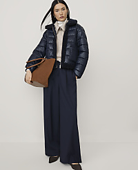 A woman wearing a navy puffer jacket and wide-leg trousers holds a brown handbag against a plain white background. carousel Product Image 3