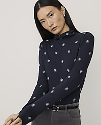 A woman wearing a navy blue patterned turtleneck and grey trousers stands against a plain, light-colored background. carousel Product Image 1