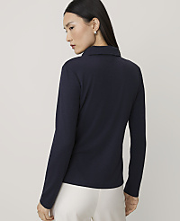 A woman wearing a navy blue long-sleeved top and white trousers stands against a plain, light grey background. carousel Product Image 2