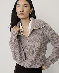 A woman wearing a textured mauve zip-up sweater over a white shirt stands against a plain light gray background. carousel Product Image 1