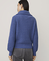 A woman wearing a blue textured knit sweater and grey pants stands against a plain light-colored background. carousel Product Image 2