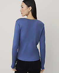 A woman wearing a blue long-sleeved shirt and black pants stands against a plain, light-colored background. carousel Product Image 2
