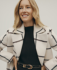 A smiling blonde woman wears a white grid-patterned coat over a black ribbed top and belt against a plain light gray background. carousel Product Image 2