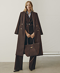 A woman wearing a brown coat and matching suit stands holding a brown handbag against a plain white background. carousel Product Image 3