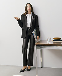 A woman wearing a black blazer, white shirt, and leather trousers stands beside a wooden table against a plain white wall. carousel Product Image 7