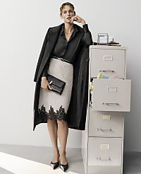 A woman in a black blouse, lace-trimmed skirt, and long coat stands next to a grey filing cabinet against a plain white background. carousel Product Image 4