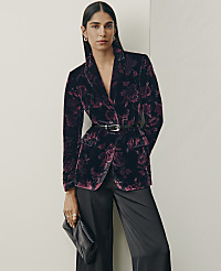 A woman wearing a floral purple velvet blazer and black trousers stands against a plain white wall. carousel Product Image 5
