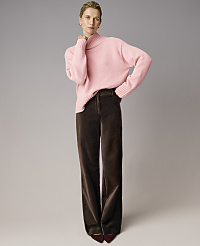 A woman wearing a pink turtleneck sweater and wide-leg brown trousers stands against a plain grey background. carousel Product Image 4