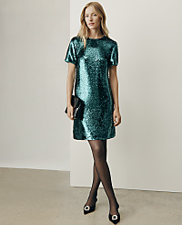 A woman wearing a shimmering green sequined dress, black tights, and black heels stands against a plain white wall. carousel Product Image 4